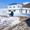 Two people in front of a white two storey building, on snowy rocky ground