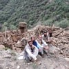Four men sitting next to a completely collapsed building in Kunar Valley, Afghanistan