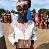 Ajok Deng, a woman in South Sudan wears a white dress, holding some cash. Behind her is a queue of people