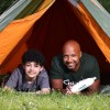 Two people, a man and an older child, in a tent outside looking straight ahead