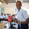 A young woman in a classroom standing beside a microscope.