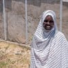 Woman smiling, stand outside wearing a white and grey striped head scarf