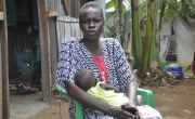 Woman sits outside hut cradling a baby girl in her arms
