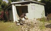Man sweeps up debris in front of his house, which is collapsing following the earthquake in Haiti