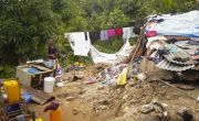 Woman stands beside clothes line full of washing to the left of her destroyed home