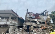 Two people stand in front of a tall building that has been reduced to rubble during the Haiti Earthquake on August 14 2021
