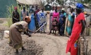 Group of women watching woman using hoe in garden