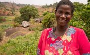Farmer Lucia Tebulo, smiling and wearing pink patterned dress in Malawi field