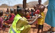 Nurse in hi-vis jacket wrapping band around arm of child in Marsabit, Kenya