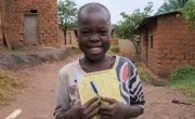 Smiling child in Burundi holding workbook and pen