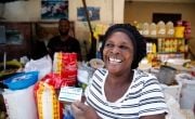 Estelle Adolphe, a participant in the USAID funded Manje Pi Byen program, uses her account to buy essential provisions from a vendor at a street market in Cité Soleil, Port-au-Prince, Haiti.