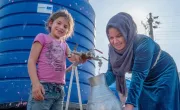 Darine* and her daughter show us the water tank, distributed and installed by Concern through the ECHO programme. (Photo: Gavin Douglas/Concern Worldwide)