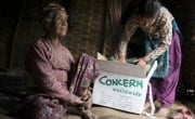 Ratna Khatri, 88 years of age and a previous survivor of the devastating 1934 earthquake, sits in the makeshift shelter her family have built since their home was destroyed in the earthquake as her granddaughter goes through the box of supplies that Concern distributed. Photo: Brian Sokol/Panos Pictures/Concern Worldwide