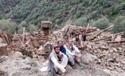 Four men sitting next to a completely collapsed building in Kunar Valley, Afghanistan