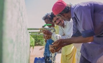 Two local men, Naaju and Rajesh are talking to each other happily while drinking water from water plant installed by Concern Worldwide. Photo: Black Box Sounds/ Concern Worldwide.