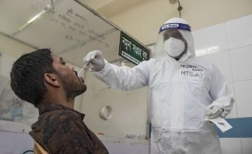 A man in PPE takes a sample collection from a patient in Bangladesh