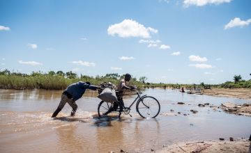 Men pushing a bicycle through floodwaters from Cyclone Idai in Mozambique