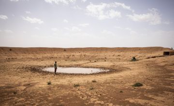 Man standing by nearly dry dam in middle of desert 