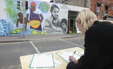 Woman signing petition across the road from mural on wall