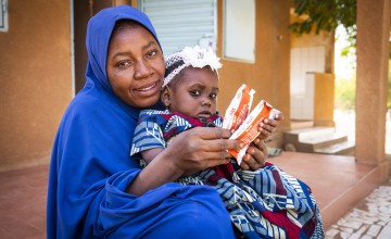 Nigerien mother and her baby holding packets of ready-to-use therapeutic food (RUTF)