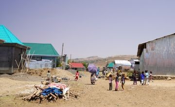 Children standing on ground amidst huts
