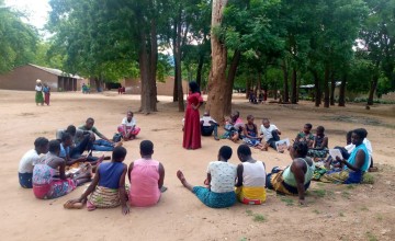 Woman standing in centre of circle, surrounded by sitting people