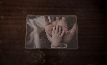 Photograph on table of baby's hand atop adult's hand