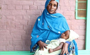 Sudanese woman in blue head scarf with sleeping child on her lap