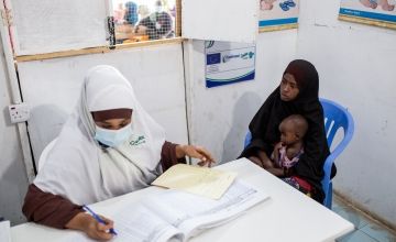 Doctor in face mask fills out notes during appointment with mother and baby in health clinic in Somalia