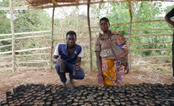 Farmers Foster and Annie (who is holding a baby) kneel at their nursery of planting tubes in Malawi