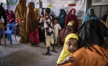 Infant girl holding onto mother's shoulder and being carried in Somalian health centre