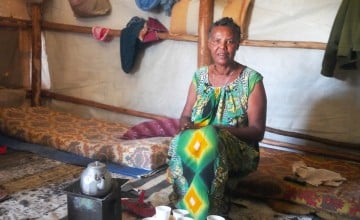 Ethiopian woman in patterned dress sitting on the floor next to kettle