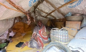 Sudanese refugee sitting on floor under tarp tent