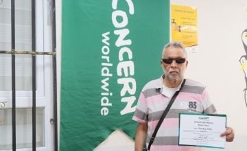 A man holds a certificate of achievement in front of a large Concern Worldwide banner