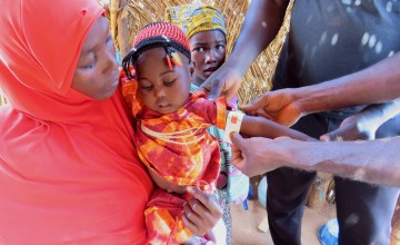 Young girl held by her mother getting her arm measured by doctor