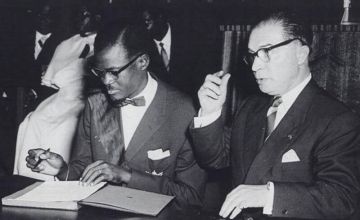 Patrice Lumumba signs the document granting independence to present-day Democratic Republic of Congo next to Belgian Prime Minister Gaston Eyskens (Photo: Congopresse / Wikimedia Commons)