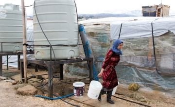 A Syrian refugee woman carries two buckets full of water at an informal tented settlement in northern Lebanon