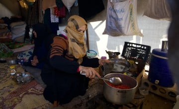 Reem* (30) prepares food for her husband Jaafar* (32) and her children inside their tent in the Ahl al-Khair camp, Syria.
