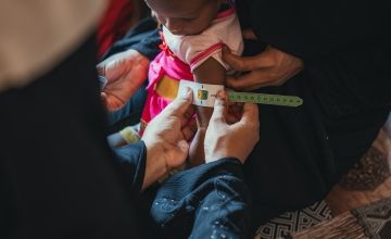 Oma, an 18-month-old girl who had suffered acute malnutrition previously, is assessed by a Community Health Volunteer, in Yemen. The MUAC band reading (green) indicates that she is a healthy weight and has recovered from malnutrition. Photo: Ammar Khalaf/Concern Worldwide