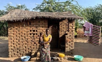 Eliza holds her baby outside her home in Bitilinyu camp