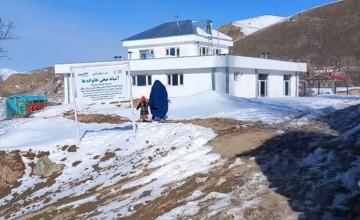 Two people in front of a white two storey building, on snowy rocky ground
