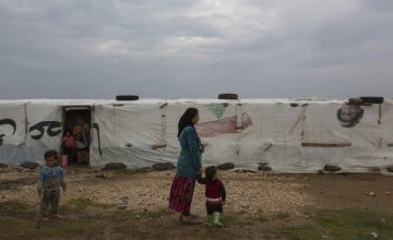 A Syrian refugee woman stands with her child in front of her tent in the village of Shir Hmyrin
