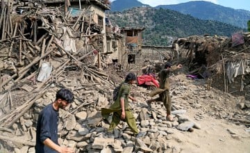 Afghans walk past houses damaged by earthquakes in Kunar province, in Eastern Afghanistan, on September 1, 2025
