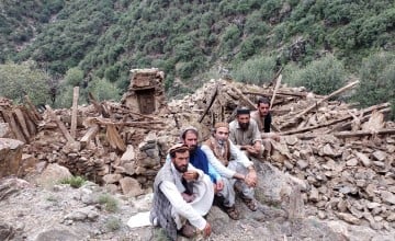 Four men sitting next to a completely collapsed building in Kunar Valley, Afghanistan
