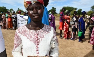 Ajok Dong, a woman in South Sudan, wears a white dress and holds some cash. Behind her is a queue of people