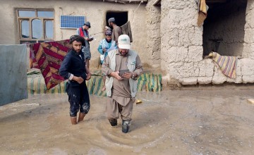 Concern staff member walking through flooded garden of a home with family members behind him