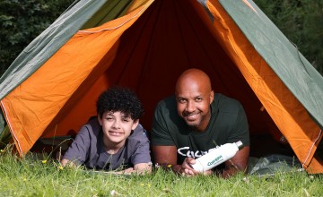Two people, a man and an older child, in a tent outside looking straight ahead