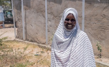 Woman smiling, stand outside wearing a white and grey striped head scarf