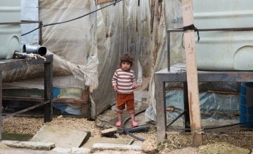 A Syrian refugee child stands next to the water tanks at an informal tented settlement in in Akkar, northern Lebanon. Photo taken by Dalia Khamissy / Concern Worldwide.