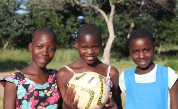 Three young woman holding a soccer ball.